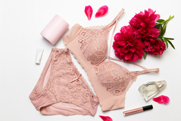 Female elegant pink lace bra, flat peony, lipstick, hand cream and barrette on a white background, flat lay.