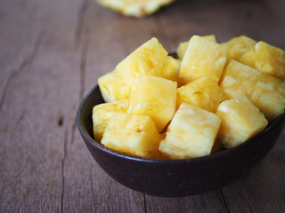 Close up of sliced pineapple chunks in a dark bowl on a wooden table.