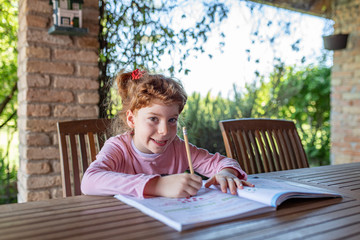 Bambina che fa i compiti di scuola, sorridente e contenta con i capelli rossi ricci, in una...