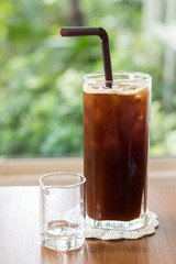 Ice americano black coffee on wooden table with nature bokeh background