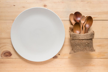 Empty white round dish or plate on wooden background, top view of tableware with copy space, different kind of spoons