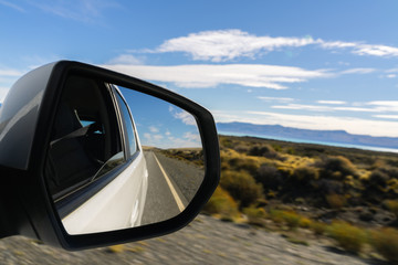 Fototapeta premium Look at side or rear mirror while driving on street in summer with golden plant leaves with sunshine blue sky