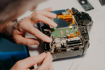 Technician engineer repairs broken photo camera with special tool. Photographer busy with...