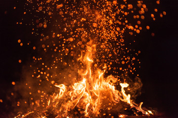 Fototapeta na wymiar Burning red hot sparks fly from big fire. Beautiful abstract background on the theme of fire. Burning coals, flaming particles flying off against black background.