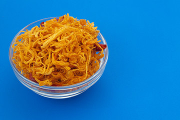 Dried shredded chicken meat in bowl on blue background with space for text