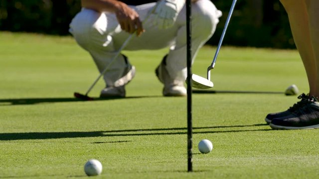 Golf instructor guiding golfer to putt ball towards hole on green