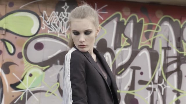 Young fashionable woman with a ponytail posing against the graffiti wall. Action. Beautiful girl with black eyeshadows wearing black sexy mesh jacket.