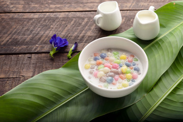 Thai sweets and colorful ball flour in a white cup on a banana leaf, coconut on an old wooden table Rainbow sweets, popular and famous Thai desserts, Bua Loi, Bua Loi, Pandan leaves
