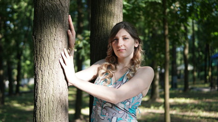 Cheerful woman with curls holding on to a tree in a park on a sunny day