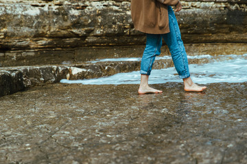 woman walking by rocky beach barefoot wet jeans