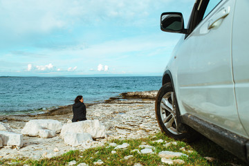 woman sitting at rock near suv car at seaside enjoying the view