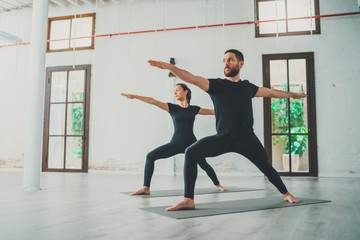 Young sportive man and woman are practicing yoga exercises in the studio. Couple of young sporty people practicing yoga lesson with partner.