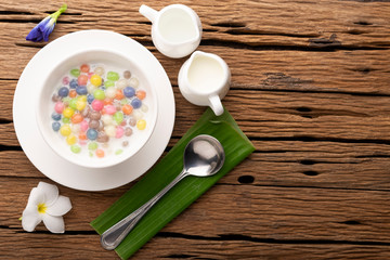 Thai sweets and colorful ball flour in a white Spoon on a banana leaf, coconut on an old wooden table Rainbow sweets, popular and famous Thai desserts, Bua Loi, Bua Loi, Pandan leaves