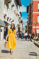 tourist woman in yellow sundress walking by small croatian city street