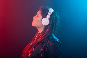 Enjoy, meloman and people concept - young woman with dreadlocks listening to the music, portrait over the dark background