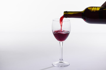 Pouring red wine into the glass on white background with copy space