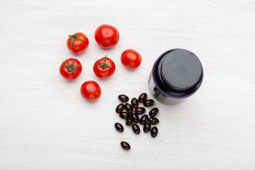 Tomatoes lie on a white table next to vitamins in the form of jelly next to a jar on a white table. Concept of vitamins and minerals.