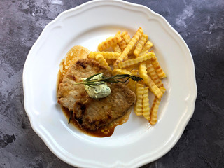 Grilled minute steak with french fries, herb butter and rosemary on stone background.
