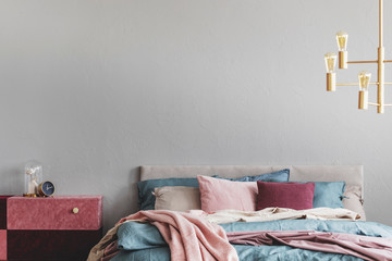 diy velvet covered pastel pink and burgundy nightstand next to warm bed with blue and beige bedding and pink pillows