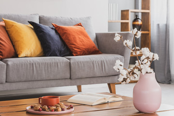 Closeup of elegant wooden coffee table in trendy living room interior with grey sofa with pillows