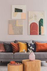 Yellow, orange, black and brown pillows on comfortable grey scandinavian sofa in bright living room interior with abstract paintings on the wall © Photographee.eu