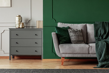 Green wall, grey Scandinavian couch and wooden chest of drawers in elegant living room interior