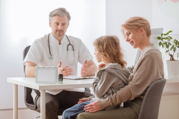 Obraz premium Mom and cute sick son in front of the handsome pediatrician's desk