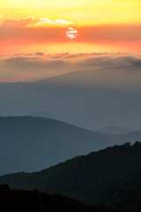 Scenic summer sunset in Caucasus mountains. Sun setting bihind clouds. Beautiful vertical landscape.