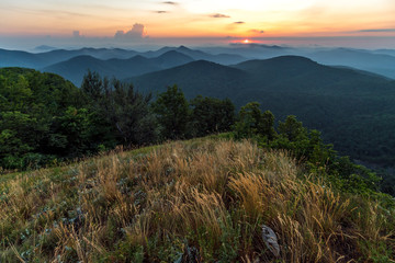 Scenic summer sunset in hazy Caucasus mountains. Sun setting bihind clouds. Beautiful landscape from top of Lysaya mountain in Tuapse district, Russia.