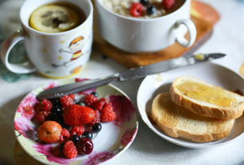 breakfast still life with oatmeal, seasonal berries, roasted toasts with lemon jam cup of tea spoon and knife