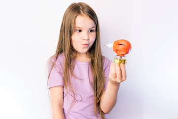 Little girl holding a fumigator from mosquitoes and looks at it against a bright background