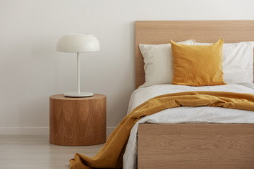 White and yellow bedding on single wooden bed in contemporary hotel interior