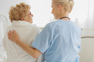 Caring doctor sitting on a hospital bed next to an senior patient and strokes her back