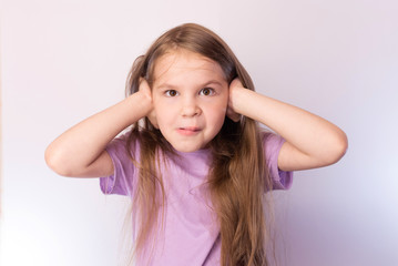 Little cute girl has closed his ears with his hands, with a funny expression on his face, on a light background