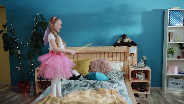 Cheerful father and daughter dressed up fancy fairies playing together on bed. Little cute girl casting a spell making her father disappear. Magic party.
