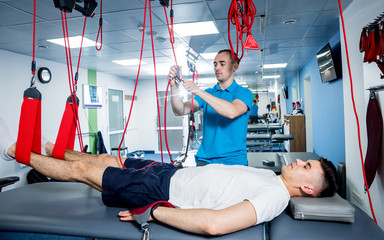 Physiotherapy. Suspension training therapy. Young man doing fitness traction therapy with...