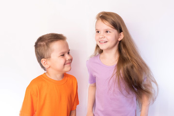 Little cute boy and girl in bright t-shirts, smiling on light background