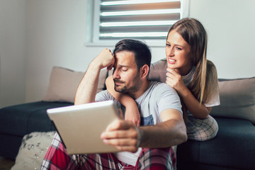 Cheerful couple using a tablet online sitting in the living room at home
