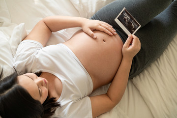 Pregnant woman feeling happy at home while taking care of her child. The young expecting mother...