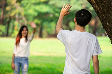 Young people, man and woman greeting or saying goodbye by waving hands in the park.