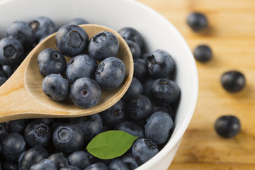 Tasty blueberries in wooden spoon, above white bowl with fresh forest fruits