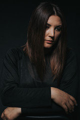 Fototapeta premium Low key studio portrait of women in her thirties looking down - arms crossed.