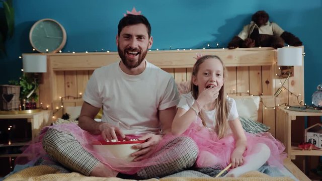 Funny daughter and dad eating throwing pop corn into camera. Portrait of happy daddy and his girl dressed like fairies having fun during costume family party.