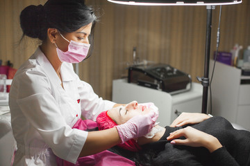 Cosmetologist making face care procedure. Specialist applying face mask to her client. Dermatology...