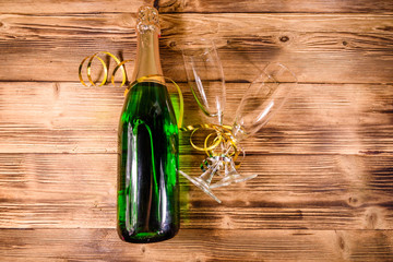 Bottle of champagne and two wineglasses decorated with golden ribbon on wooden table. Top view