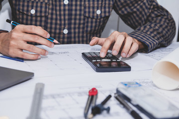 Concept architects, Hand of asian young man engineer using calculator for calculation number of structural materials architects On the desk with a blueprint in the office.