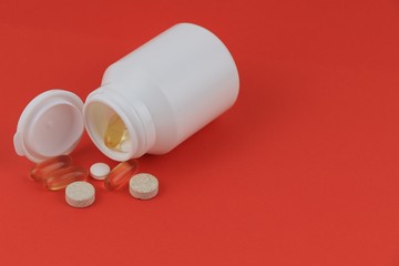 Pills pills in a white jar loose on a red background.