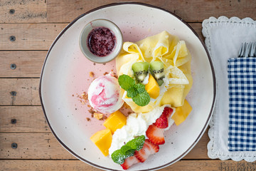 Crepe and ice cream with fresh fruit on wooden table.