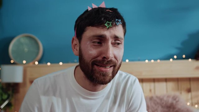 Portrait of miserable man wearing hairpins and crown crying for help on camera. Pretty girl dressing his daddy for the party posing in the studio.