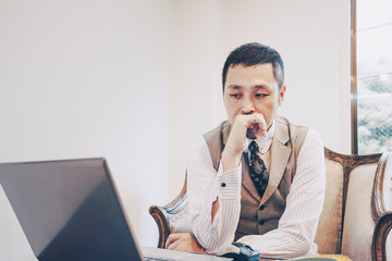 ノートパソコンの前で考え事をする男性